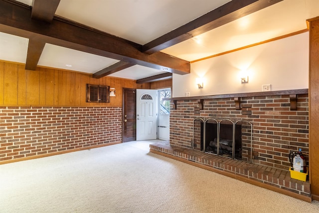 unfurnished living room with beamed ceiling, carpet floors, a brick fireplace, and wood walls