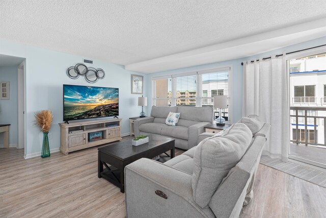 living room featuring a textured ceiling, light wood finished floors, baseboards, and visible vents