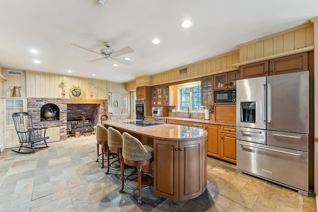 kitchen with stone tile floors, a ceiling fan, a kitchen island, a sink, and stainless steel appliances