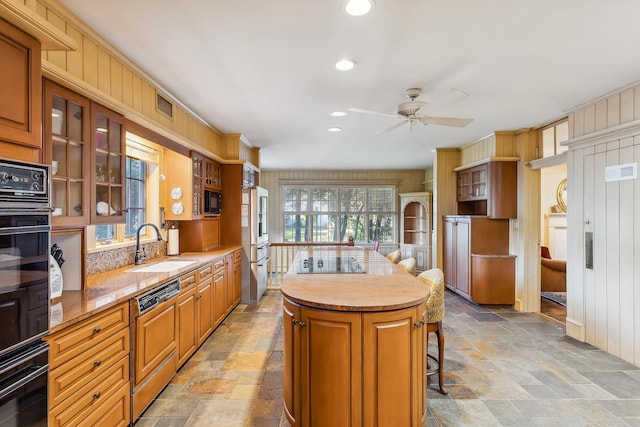kitchen featuring stone tile flooring, a sink, a kitchen island, and black appliances