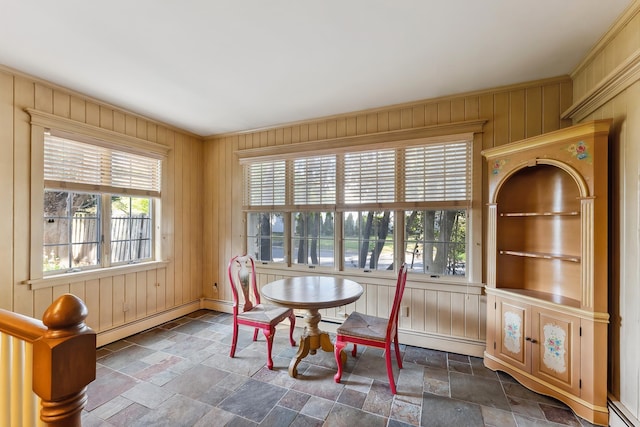dining area featuring wooden walls, ornamental molding, a baseboard radiator, and stone tile flooring