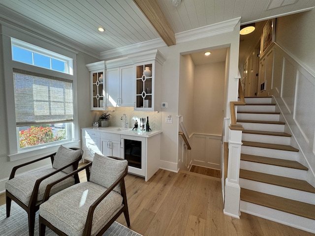 bar featuring light wood-type flooring, ornamental molding, wooden ceiling, beamed ceiling, and white cabinetry