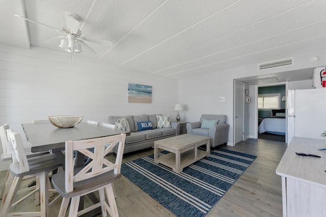 living area featuring ceiling fan, light wood-style flooring, a textured ceiling, and visible vents