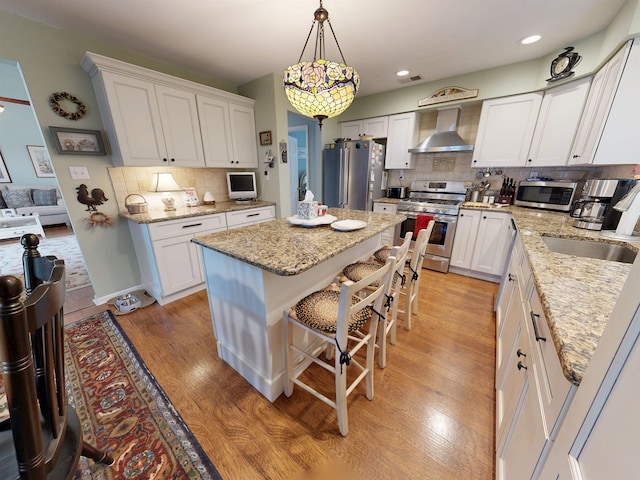 63 Cape Woods Rd, North Cape May, NJ 08204 - kitchen featuring wall chimney range hood, stainless steel appliances, backsplash, white cabinetry, and hanging light fixtures
