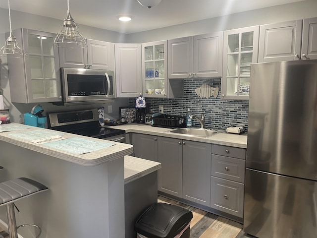 kitchen with sink, hanging light fixtures, stainless steel appliances, a breakfast bar area, and gray cabinets