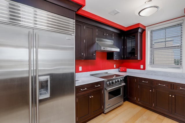 kitchen featuring high end appliances, light wood-type flooring, and exhaust hood