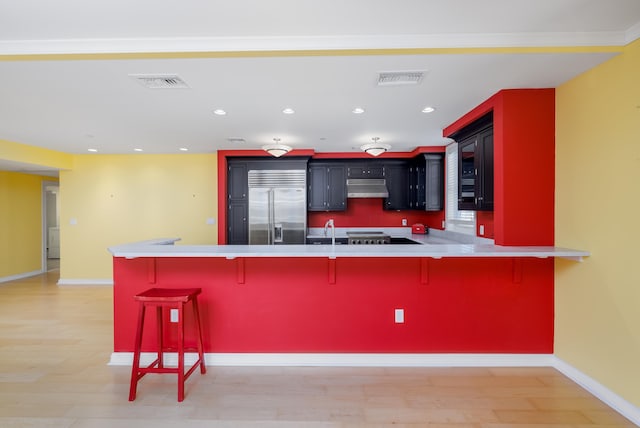 kitchen with a kitchen bar, kitchen peninsula, sink, light hardwood / wood-style flooring, and built in refrigerator