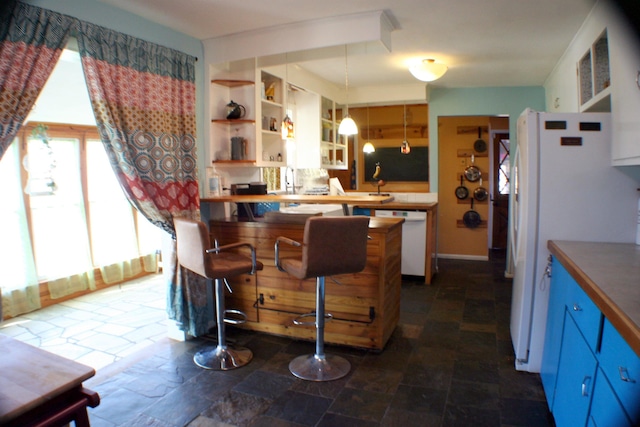 kitchen featuring blue cabinetry, open shelves, hanging light fixtures, stone finish floor, and white appliances