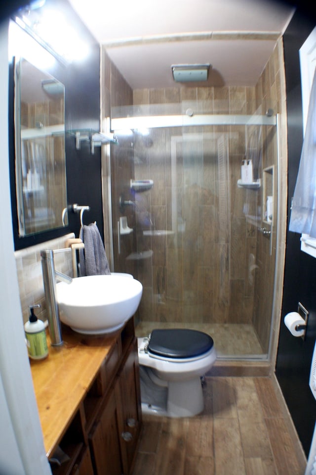 bathroom with tasteful backsplash, toilet, wood finished floors, vanity, and a shower stall