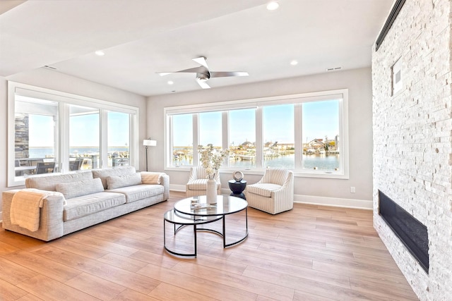 living room featuring recessed lighting, a stone fireplace, light wood-style flooring, and baseboards