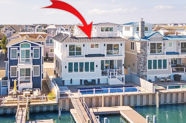 rear view of property with a water view, a standing seam roof, metal roof, fence, and a residential view