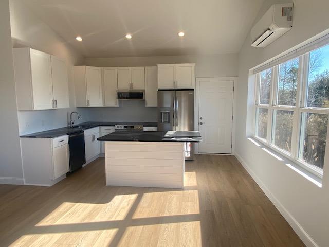 kitchen featuring stainless steel appliances, white cabinetry, a wall mounted air conditioner, and light wood-type flooring