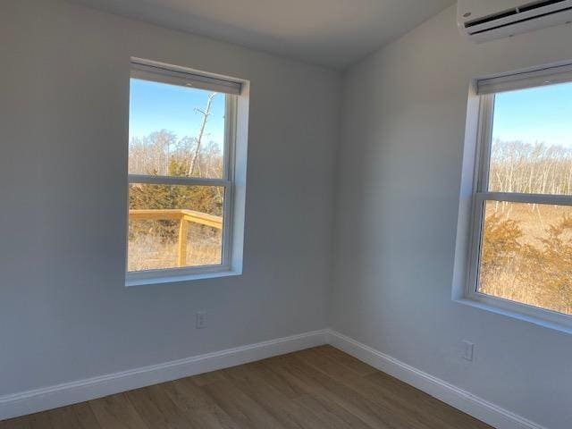 empty room with an AC wall unit, hardwood / wood-style floors, and a wealth of natural light