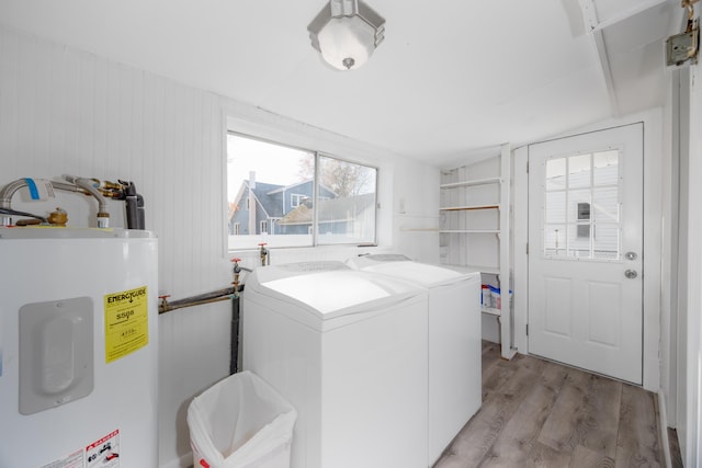 laundry area featuring water heater, light hardwood / wood-style flooring, wooden walls, and independent washer and dryer