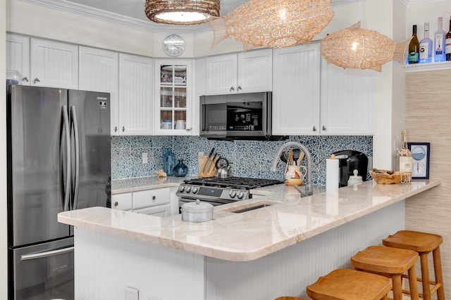 kitchen with white cabinetry, kitchen peninsula, a kitchen bar, decorative backsplash, and appliances with stainless steel finishes