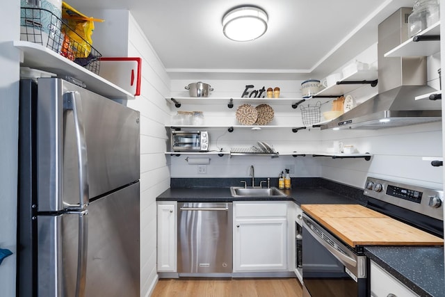 kitchen with wall chimney range hood, sink, light wood-type flooring, white cabinetry, and stainless steel appliances