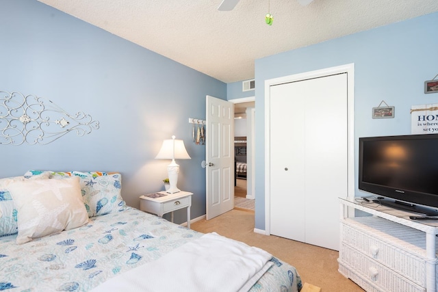 bedroom with ceiling fan, a closet, light carpet, and a textured ceiling