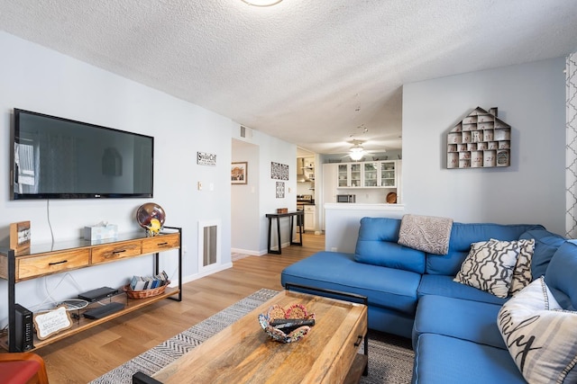 living room with ceiling fan, built in features, a textured ceiling, and hardwood / wood-style flooring