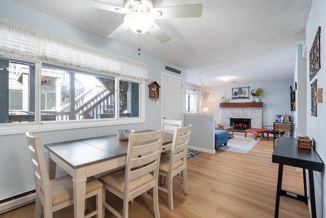 dining area featuring a baseboard heating unit, ceiling fan, a textured ceiling, a fireplace, and light hardwood / wood-style floors