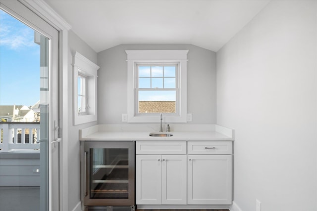 bar with wine cooler, baseboards, vaulted ceiling, and a sink