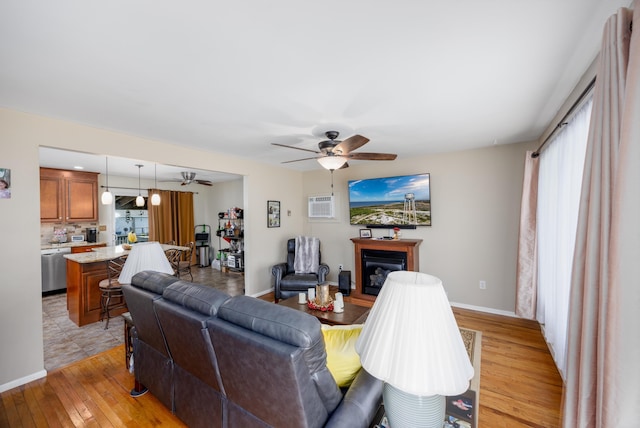 living room with a wall mounted AC, light wood-type flooring, ceiling fan, and a healthy amount of sunlight