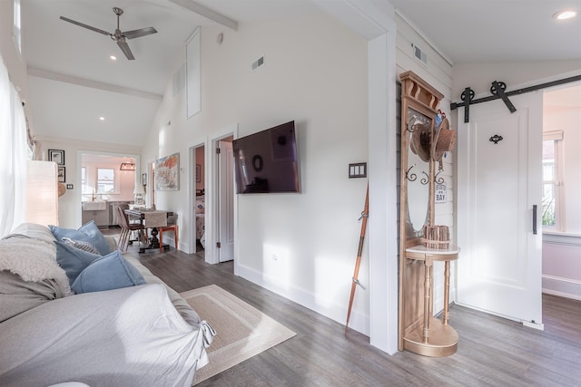 living room featuring a ceiling fan, a barn door, wood finished floors, and beam ceiling