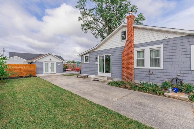 back of property with entry steps, french doors, a yard, and fence