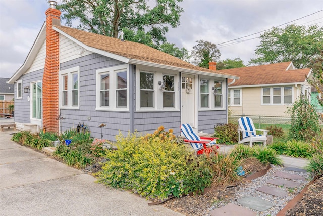 view of front of home featuring a chimney, roof with shingles, and fence