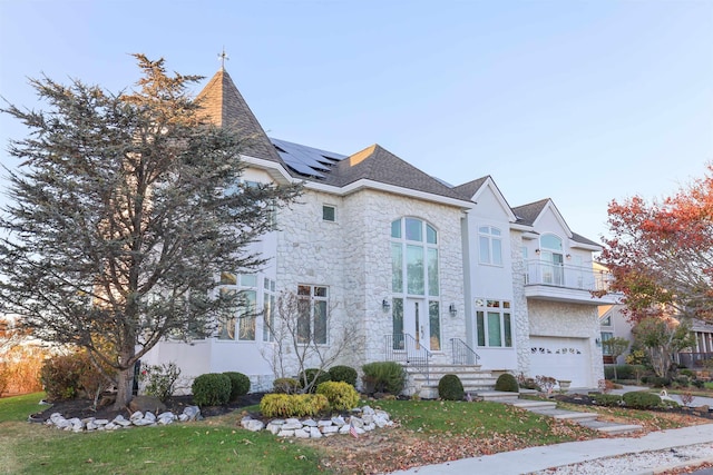 view of front of house with a front yard, solar panels, a balcony, and a garage