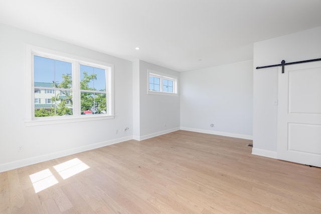 unfurnished room with a barn door and light hardwood / wood-style floors