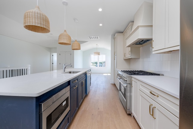 kitchen with blue cabinetry, hanging light fixtures, a large island with sink, appliances with stainless steel finishes, and custom exhaust hood