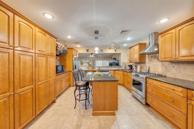 kitchen with black microwave, stainless steel range, wall chimney exhaust hood, a breakfast bar, and a kitchen island