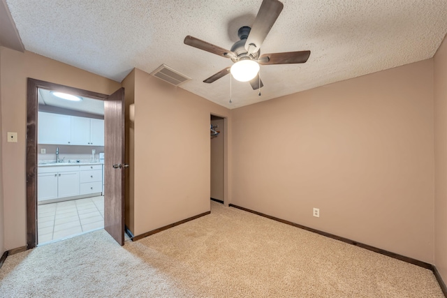 unfurnished bedroom with a textured ceiling, ceiling fan, sink, and light carpet