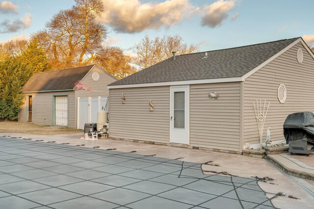 back house at dusk featuring an outbuilding, a patio, and a covered pool