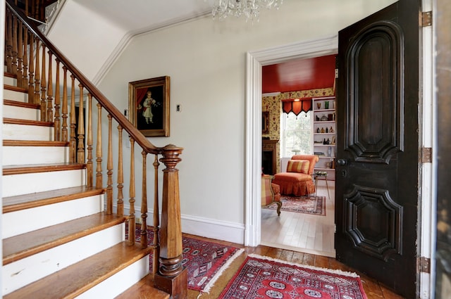 entryway featuring hardwood / wood-style flooring, a fireplace, a chandelier, baseboards, and stairs