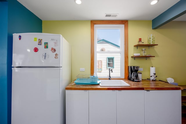 kitchen featuring visible vents, a sink, white cabinetry, recessed lighting, and freestanding refrigerator