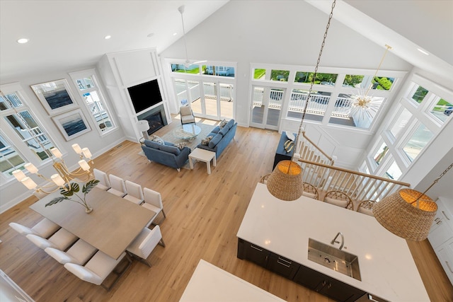 living room featuring high vaulted ceiling, a glass covered fireplace, plenty of natural light, and light wood finished floors