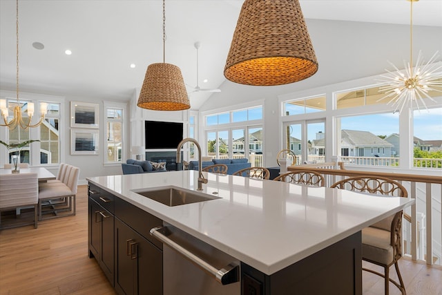 kitchen featuring hanging light fixtures, light wood-style flooring, stainless steel dishwasher, a sink, and a chandelier