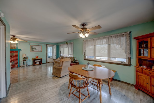 dining room with ceiling fan, a fireplace, and light hardwood / wood-style flooring