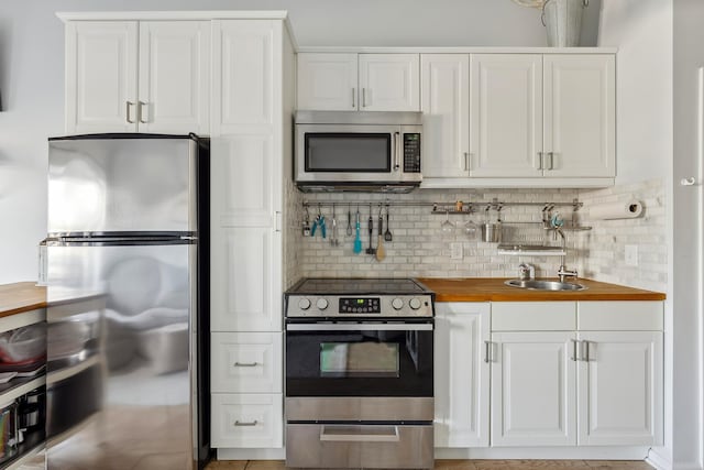 kitchen featuring backsplash, butcher block countertops, white cabinets, and appliances with stainless steel finishes