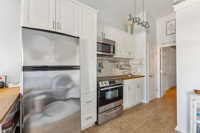 kitchen with butcher block countertops, white cabinetry, appliances with stainless steel finishes, and a sink