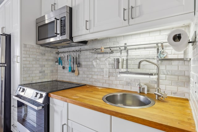 kitchen featuring range with electric cooktop, butcher block countertops, a sink, stainless steel microwave, and freestanding refrigerator