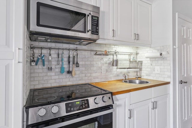 kitchen with decorative backsplash, appliances with stainless steel finishes, white cabinets, wood counters, and a sink