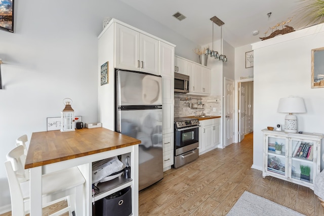 kitchen with light wood finished floors, tasteful backsplash, butcher block countertops, appliances with stainless steel finishes, and white cabinets