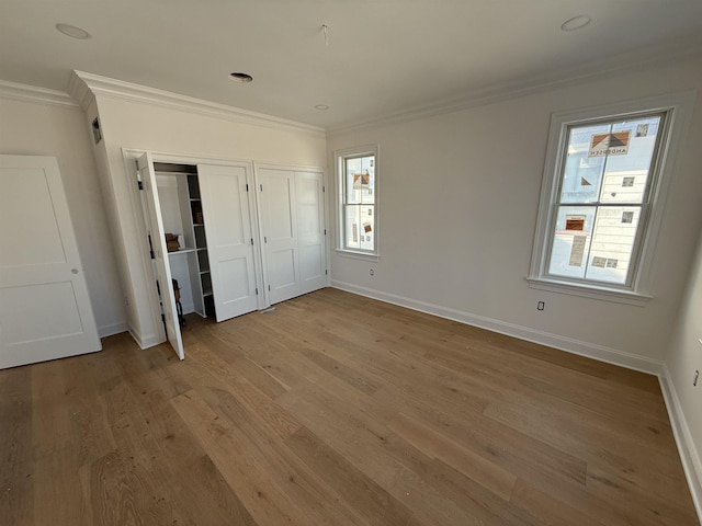 unfurnished bedroom featuring baseboards, ornamental molding, multiple closets, and wood finished floors