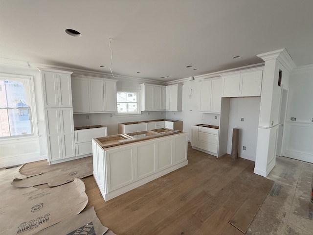 kitchen featuring wood-type flooring, a kitchen island, white cabinets, and crown molding