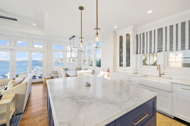 kitchen with white cabinetry, sink, a raised ceiling, pendant lighting, and a water view