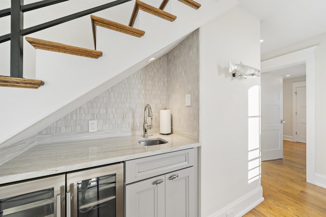 bar with sink, backsplash, beverage cooler, and light hardwood / wood-style flooring