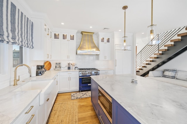 kitchen featuring wall chimney exhaust hood, hanging light fixtures, stainless steel appliances, light stone counters, and white cabinets