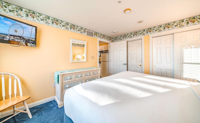 bedroom featuring multiple closets, visible vents, dark carpet, freestanding refrigerator, and baseboards